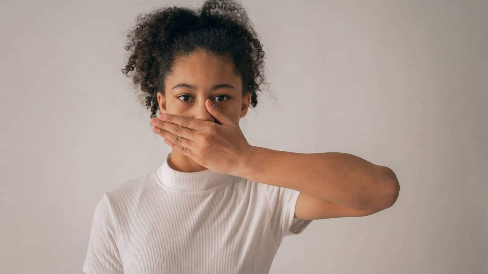 woman with curly hair in white t-shirt holding her hand sideways covering her mouth