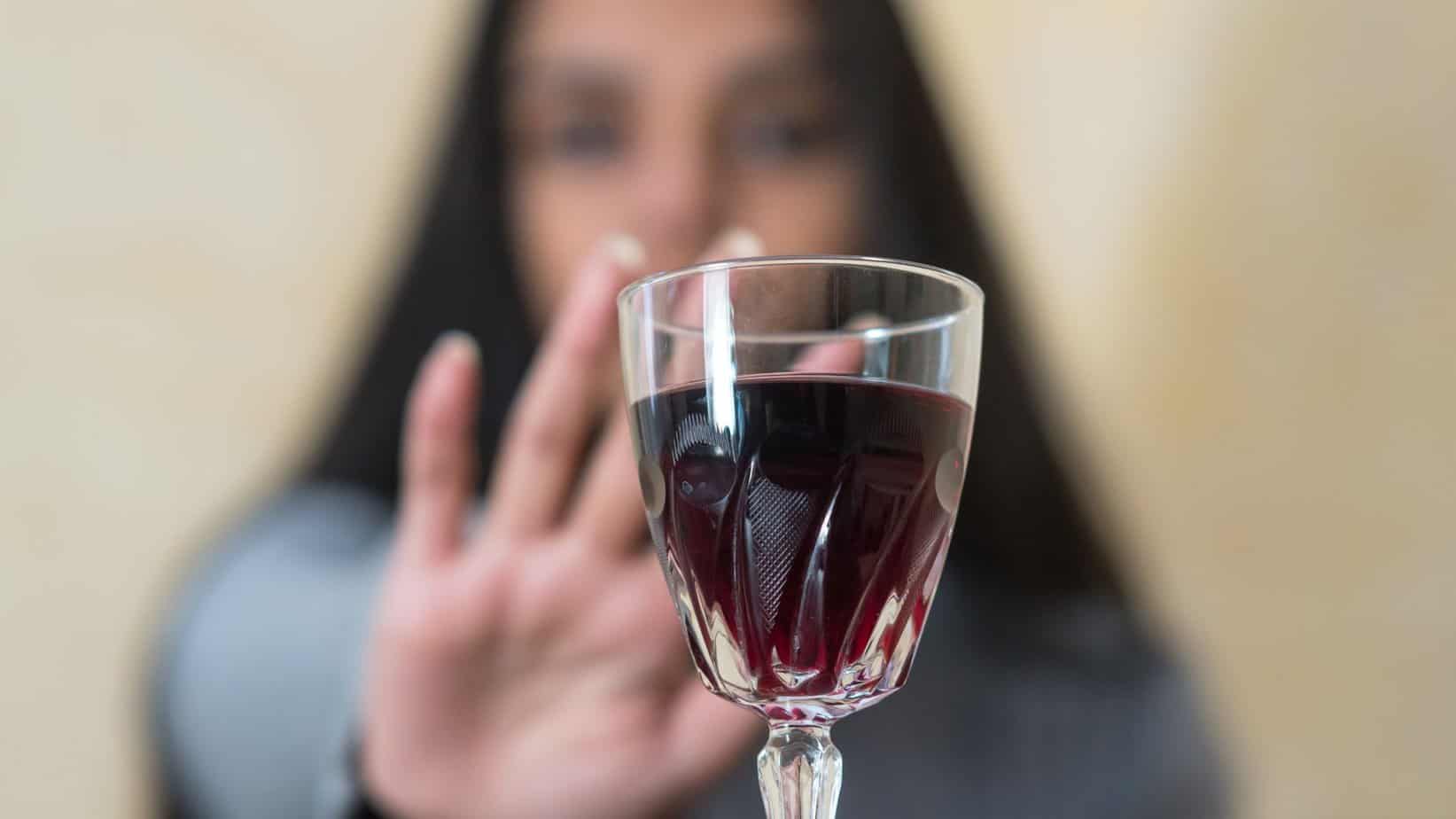 Glass of wine in front while woman behind reaches for it