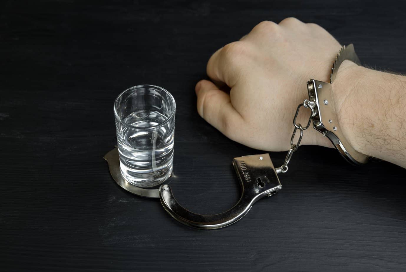 hand handcuffed to shot glass