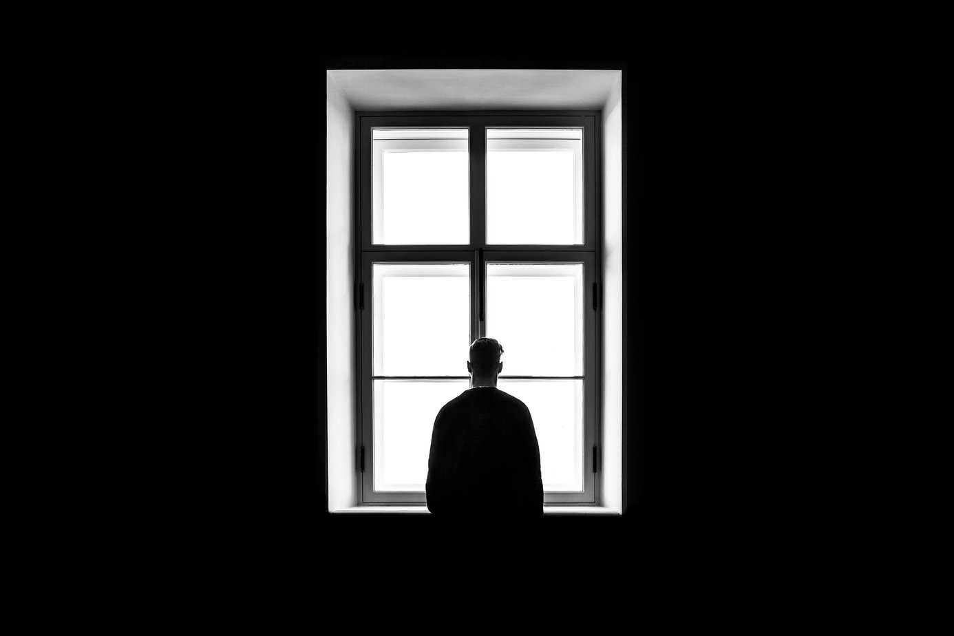 Black and white photo of man with back to camera standing in front of window